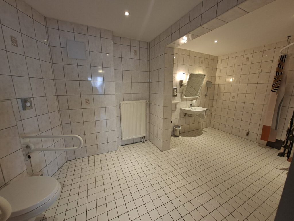 Hotel Sonne Karlsruhe, ein großzügiges barrierefreies Bad welches auch für Rollstuhlfahrer/innen geeignet ist. Haltegriffen am WC, befahrbare Dusche auch mit ausklappbarer Sitzmöglichkeit, Notrufknopf